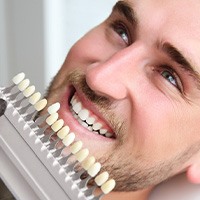 Man smiling with shade guide held to teeth