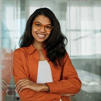 Woman in orange shirt leaning on wall in office smiling