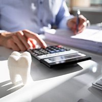 Man in buttoned shirt calculating costs at desk with model tooth