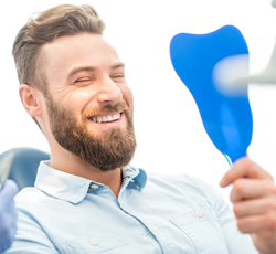 Man in dental chair looking at smile in mirror