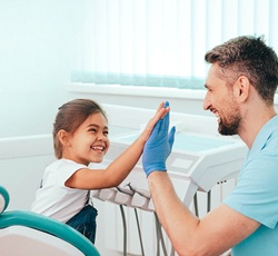 A little girl giving her dentist a high-five and smiling after receiving care from a practice offering children’s dentistry in Lovell, WY