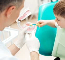 A dentist holding a mouth mold while instructing a little boy on how to properly brush its teeth