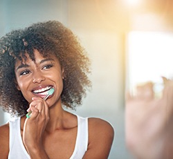 Woman smiling at reflection while brushing her teeth