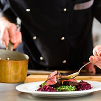 A chef pouring sauce over a steak dinner