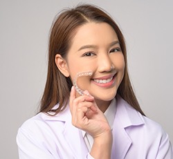 a young patient smiling and holding her Invisalign tray