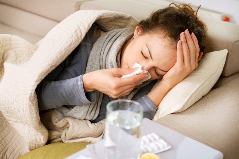 A sick woman blowing her nose and lying down.