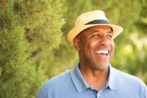 older man wearing a hat standing in front of trees